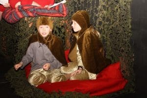 2 børn udklædt som dyr med kapper. De sidder på en rød pude